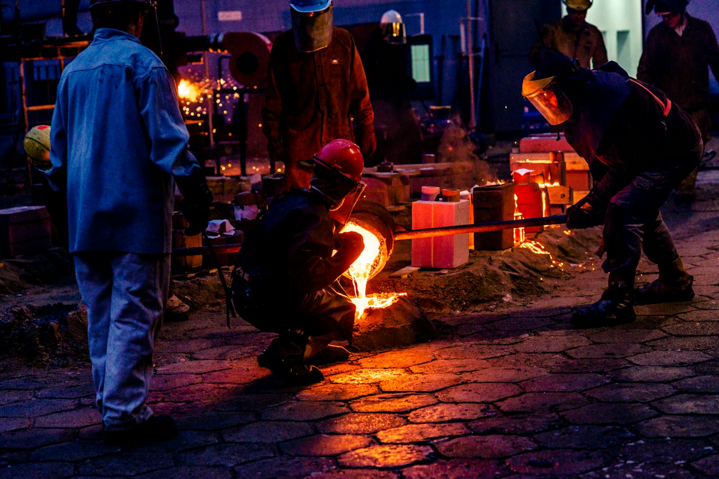 Metalworkers pour molten metal into molds during casting.